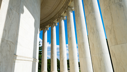  white marble Ionic columns forming the circular colonnade of the Jefferson Memorial structure against a bright blue sky with light clouds