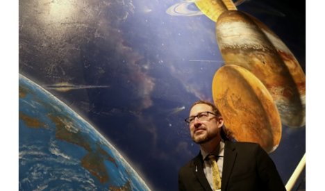 Gideon Marcus standing in front of backdrop of planets and moons