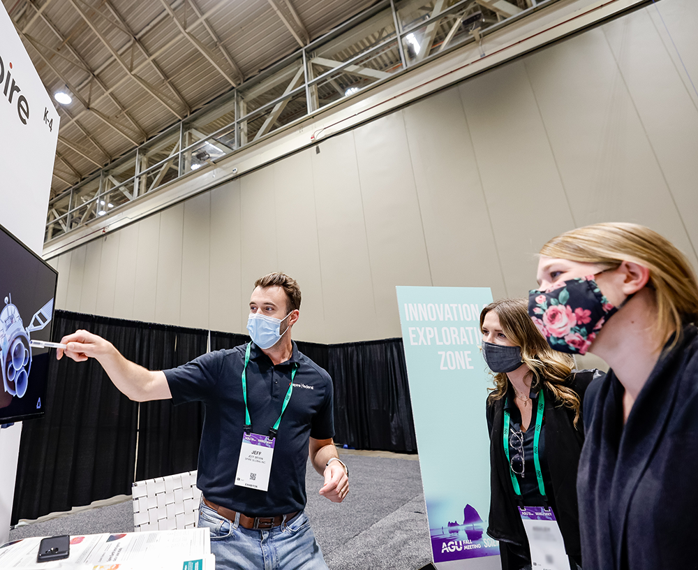 A man at AGU Fall Meeting 2021 points to a screen as two attendees observe.