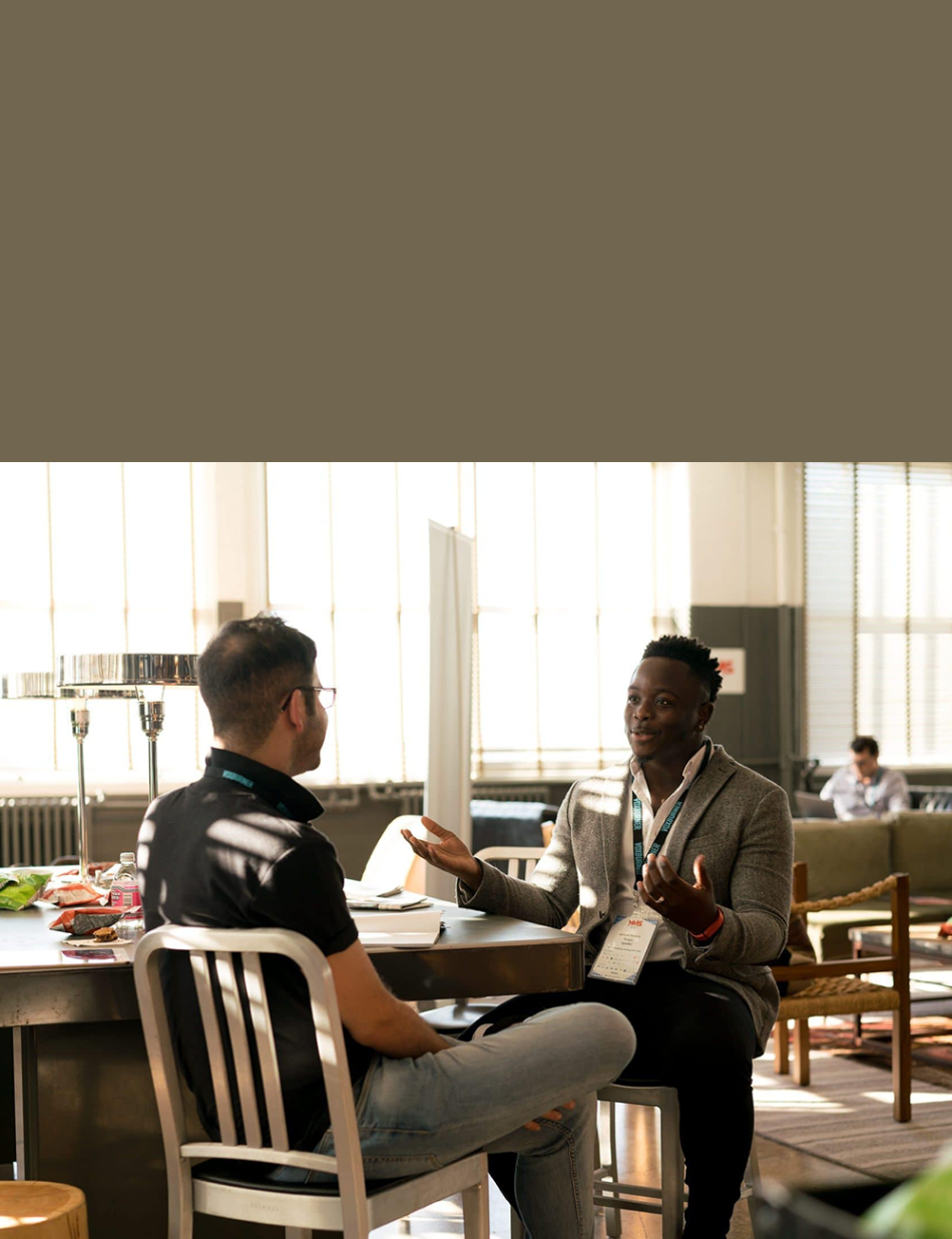 two men seated at table in sunny room conversing, mentoring