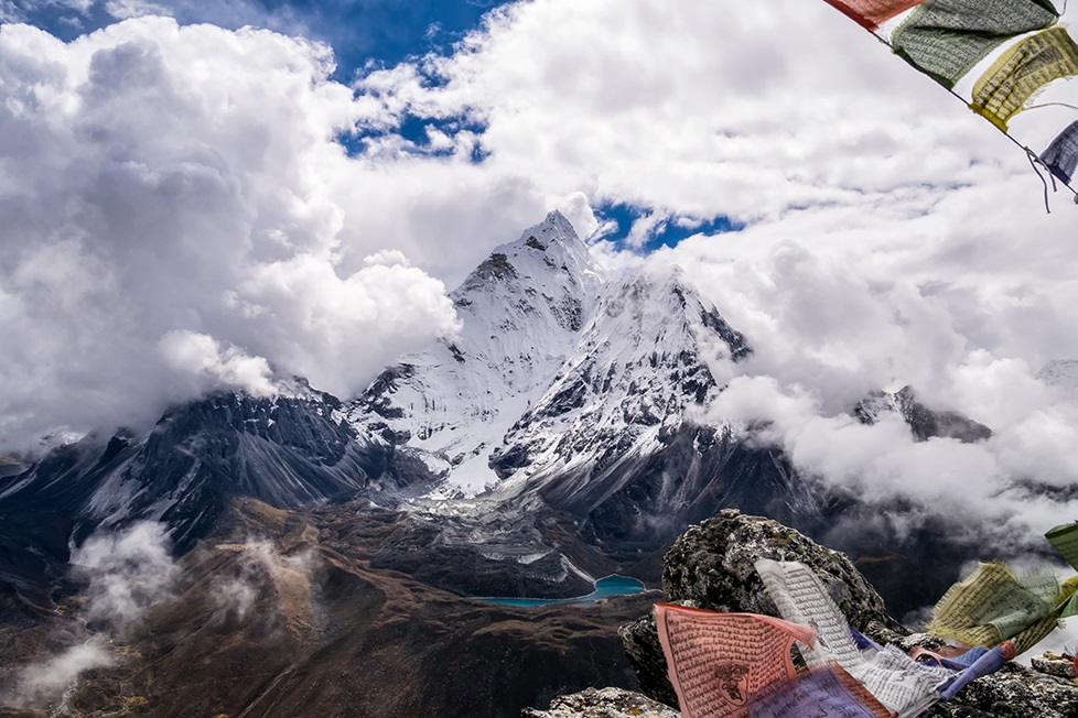 A snow-covered mountain surrounded by clouds with colorful fabric in the foreground