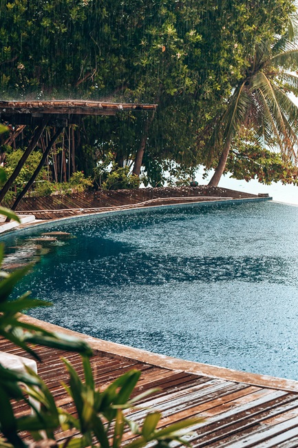Rain falls over a pool with trees in the background
