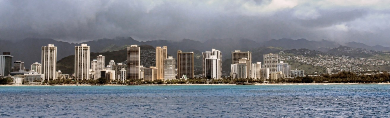 View from the ocean of sunny Honolulu skyline, with rainclouds approaching