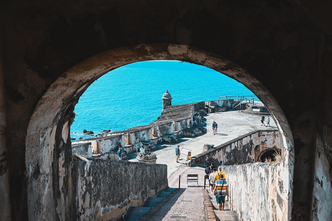 Tourists walking down an outdoor staircase at 16th century fortress in old San Juan, Puerto Rico. Sunny day, bright blue ocean.