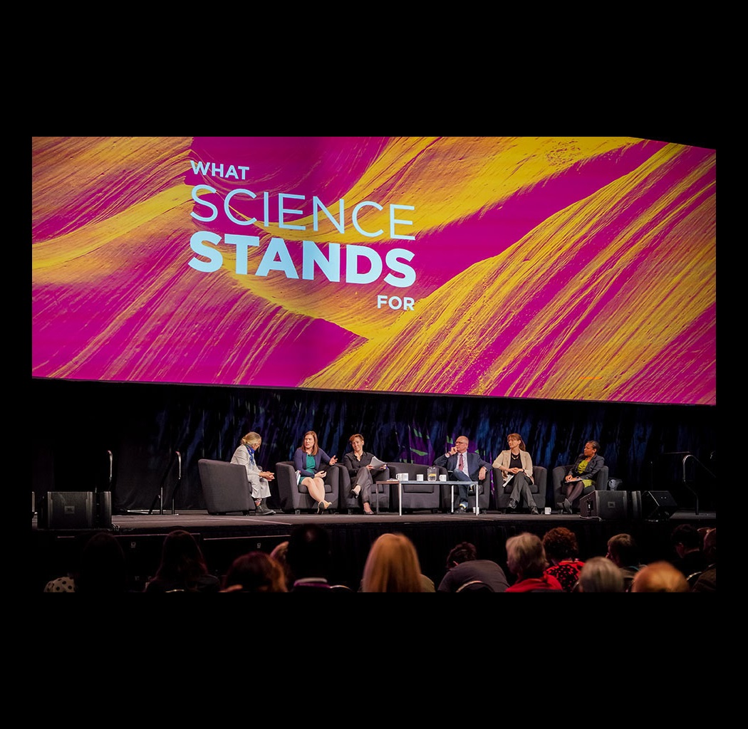 Panel session sits on stage in front of a screen that says "What Science Stands For"