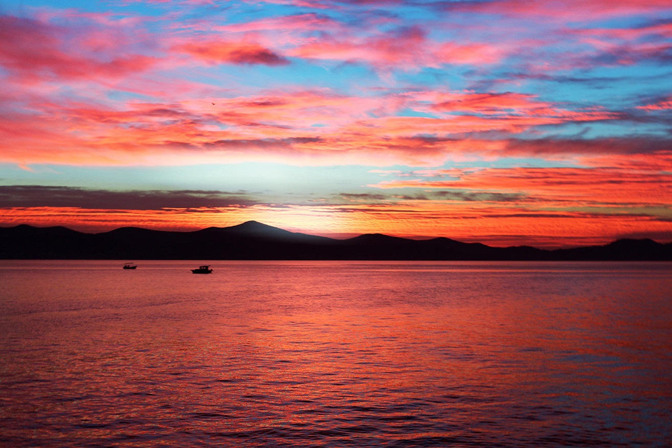 Ocean with mountains at sunset under pink clouds