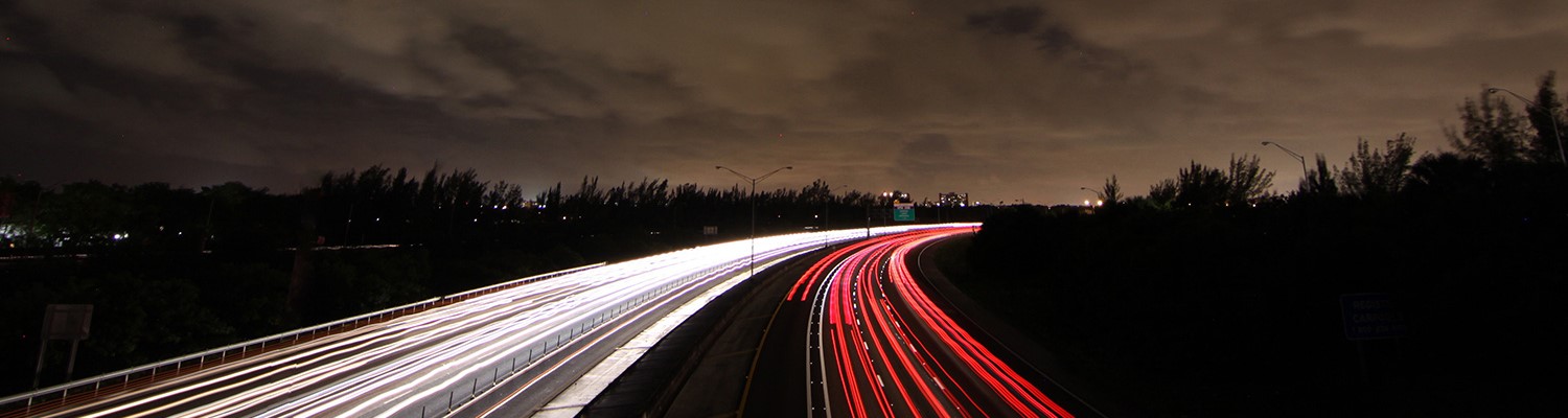 Light beams from cars on roadway under a cloudy night sky