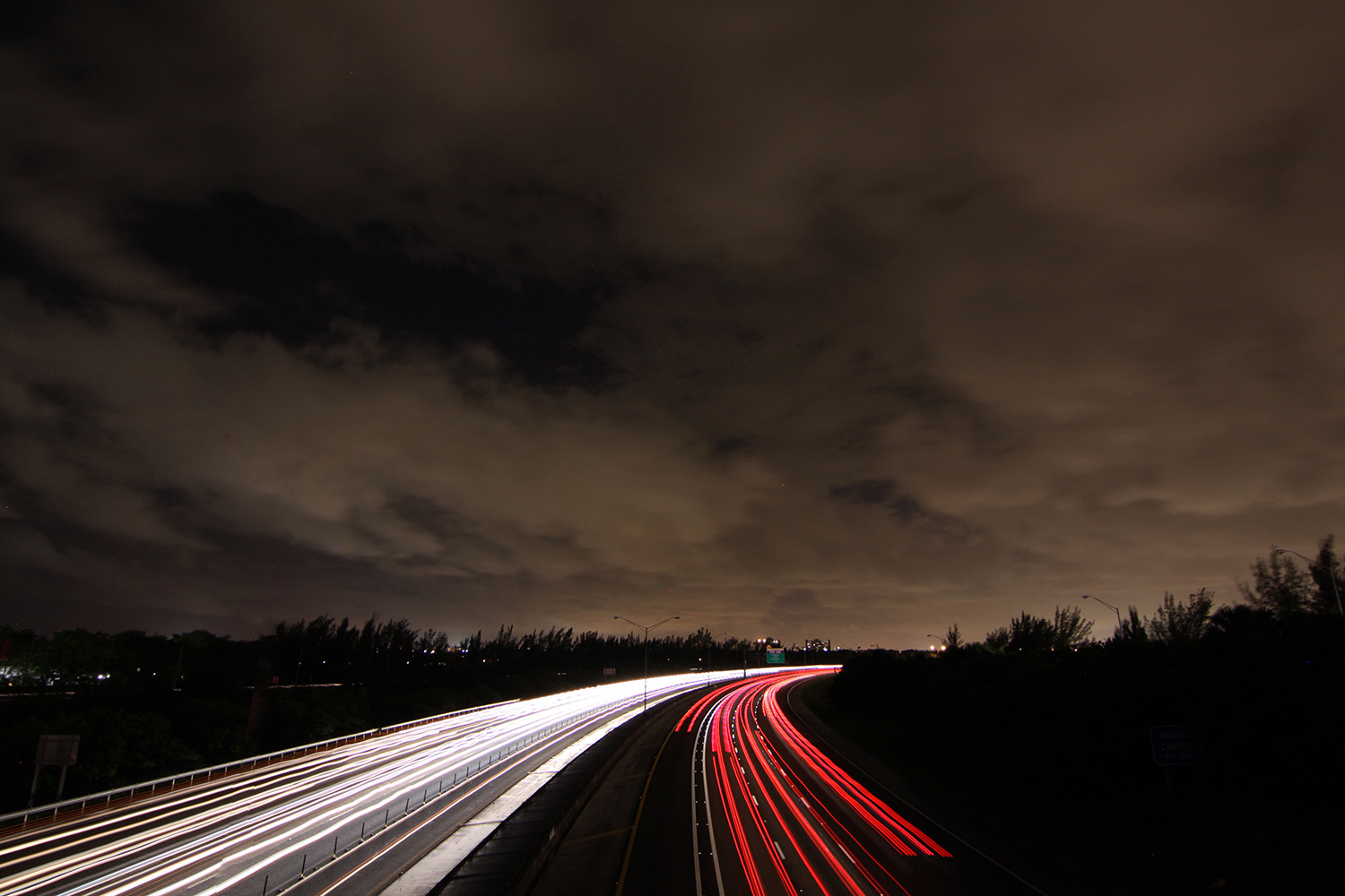 Light beams from cars on roadway under a cloudy night sky