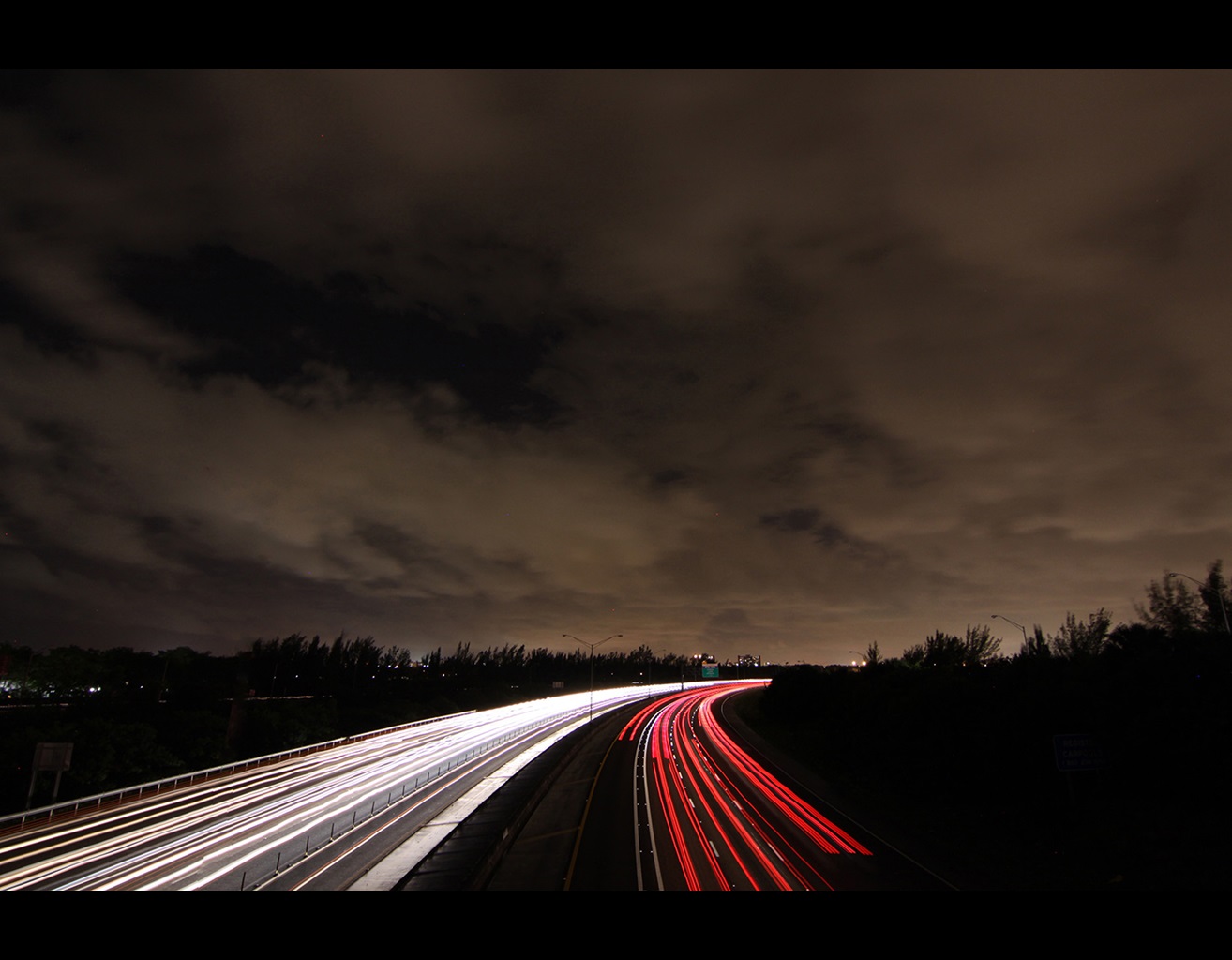 Light beams from cars on roadway under a cloudy night sky