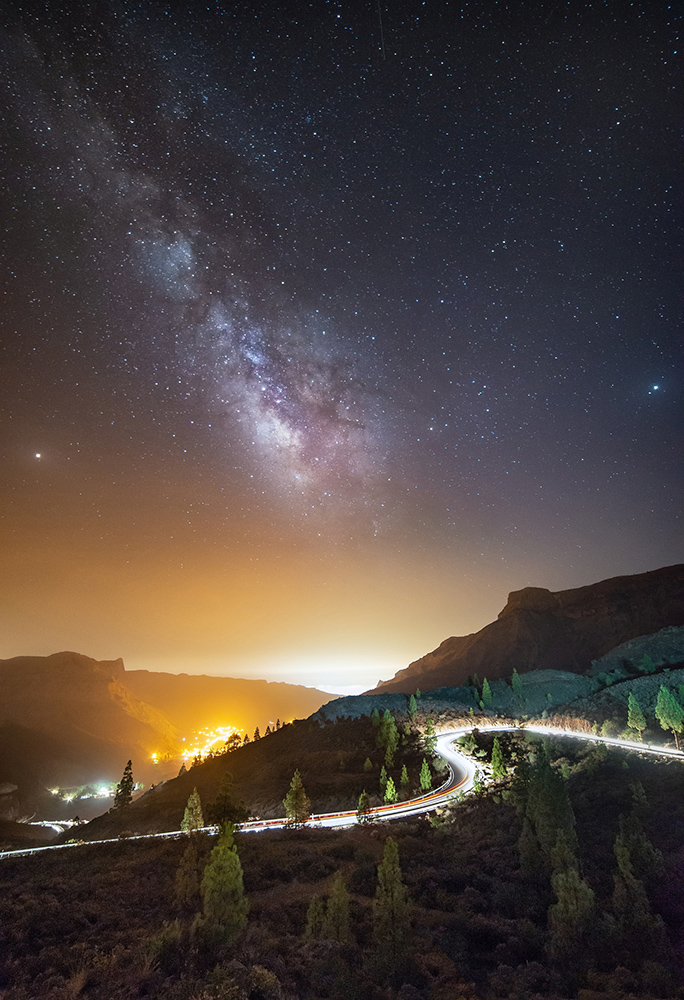 Cars driving up a curvy mountain road under a starry sky
