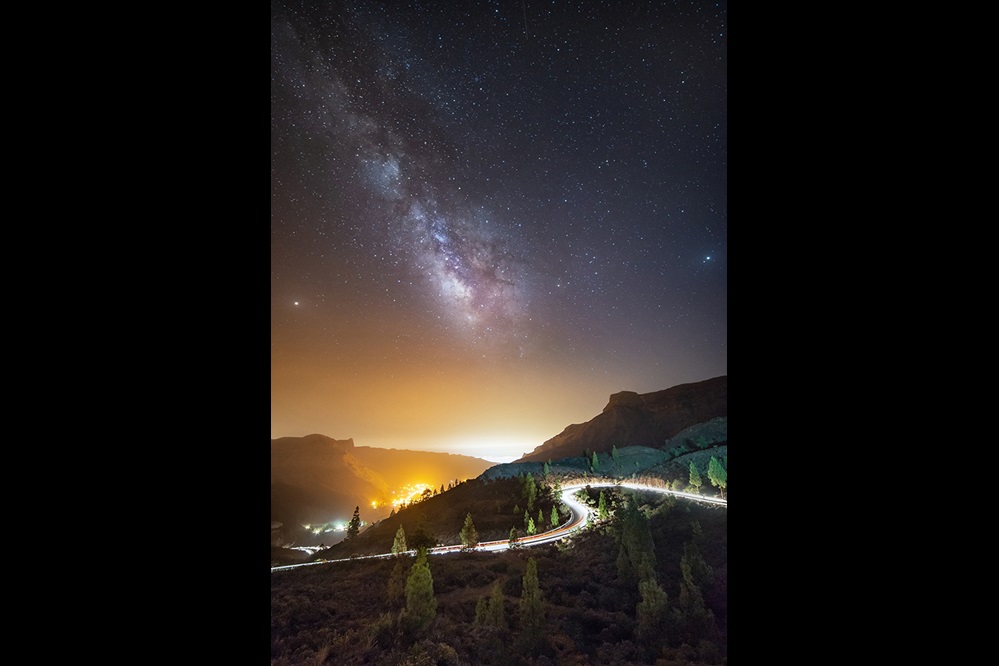 Cars driving up a curvy mountain road under a starry sky