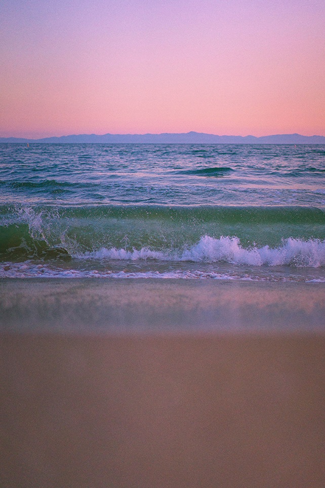 Waves crashing on shore under a pink sky at sunset