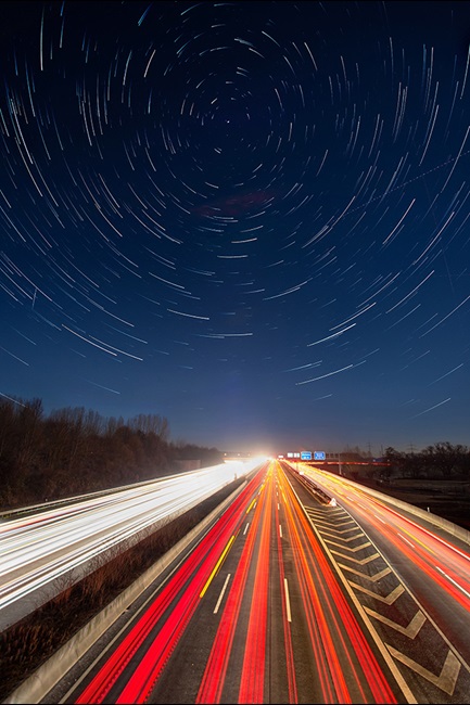 Roadway with car light beams under a circular star sky