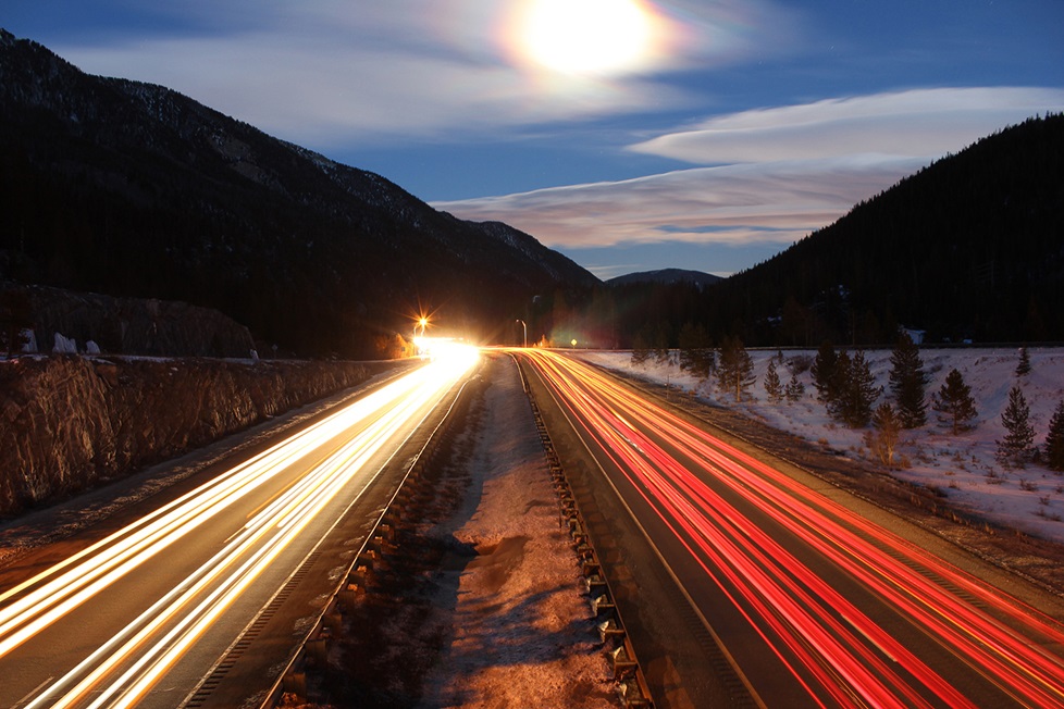 Snowy roadway with light beams under the clouds and moon