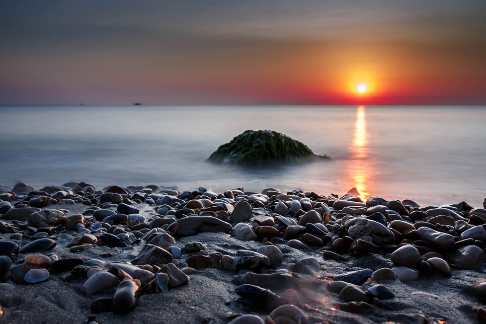 Rocks on shore line with sun reflecting on water