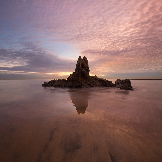 Rocky island in water under pink clouds
