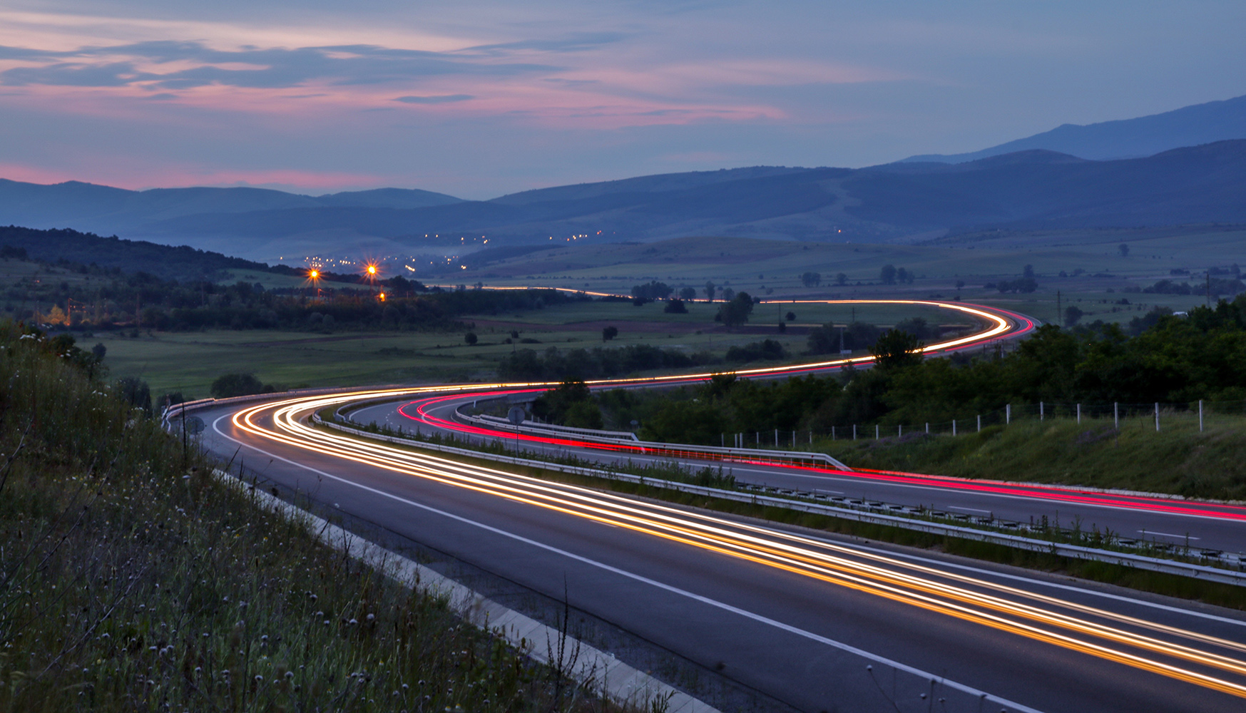 Cars driving through valley at dusk with light beams