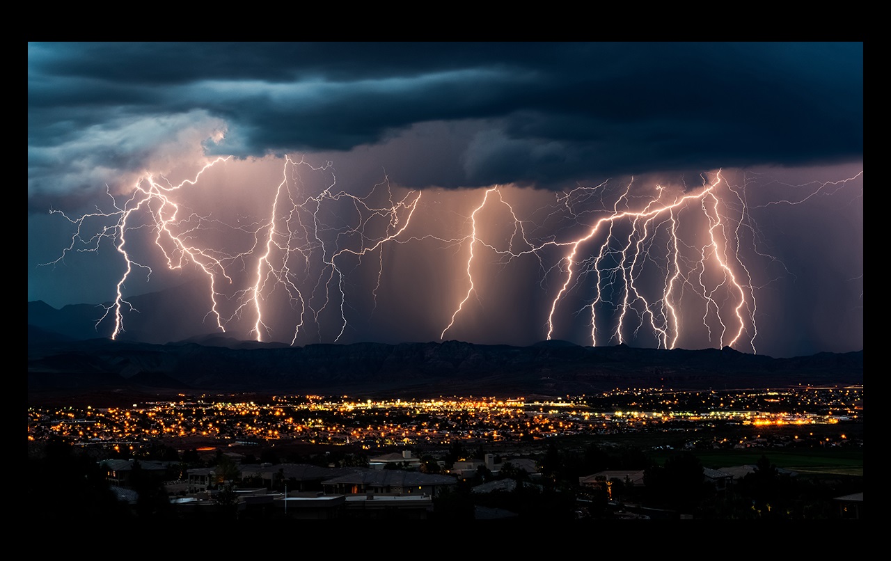 Multiple lightning strikes on a stormy evening behind a city.