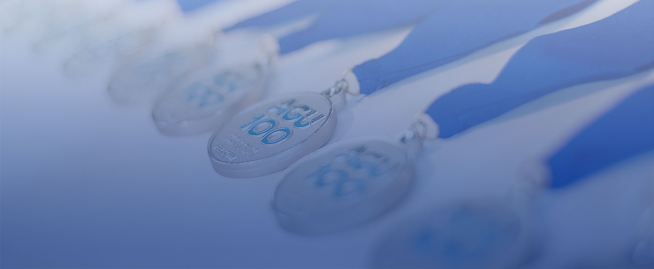 A photography of AGU Fellows medals with the AGU100 logo and blue ribbons laying across a white table. 