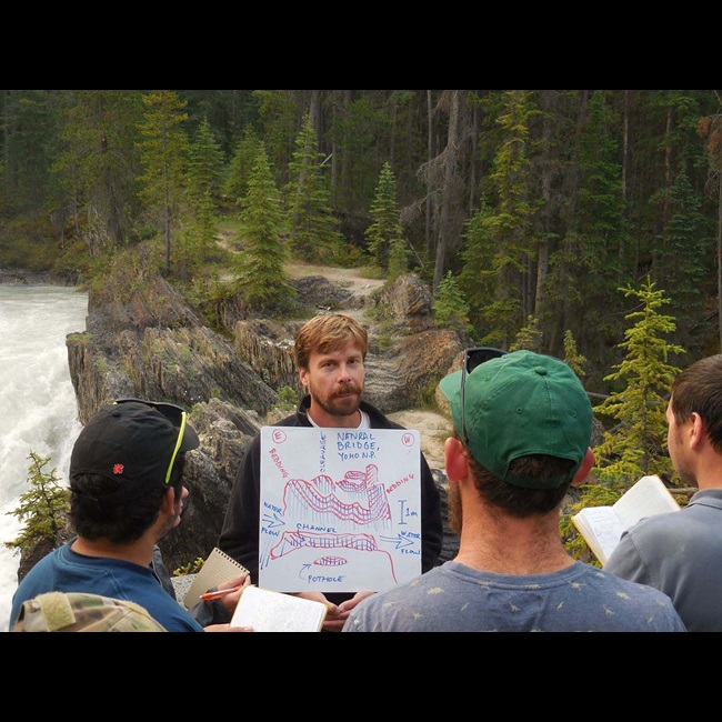 Person presenting diagram to crowd of people beside a river