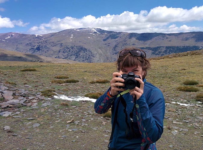 Woman smiling behind camera on top of a mountain