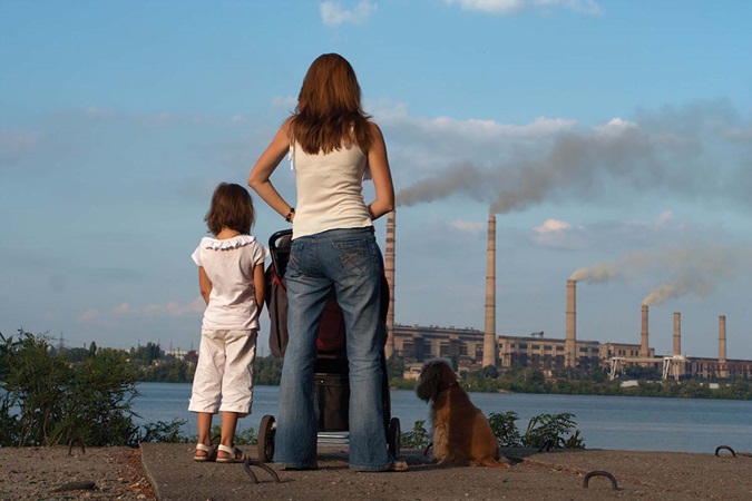 Mother with her kids and dog are looking over river and chimney-stalks polluting an air.