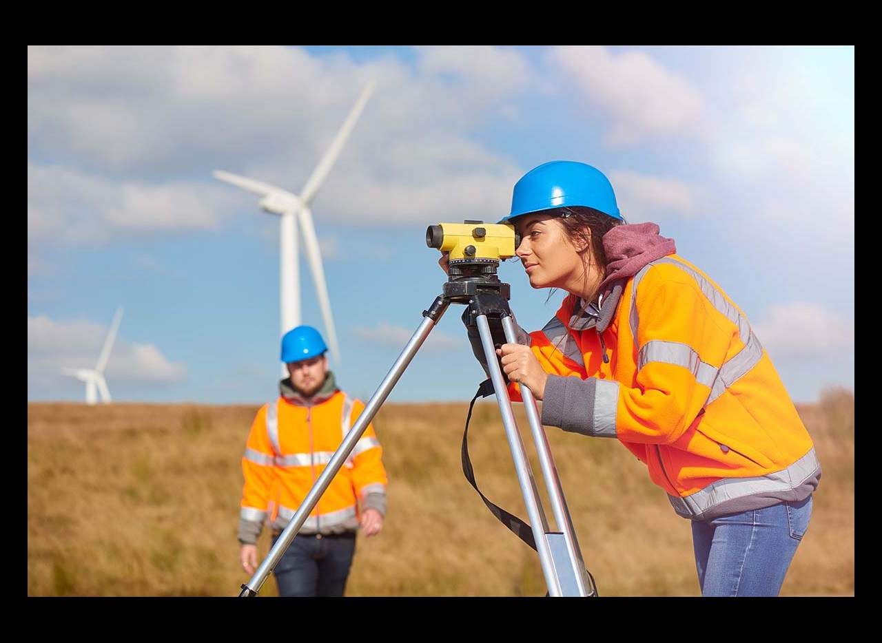 Female engineers looking through the level with wind turbines in background