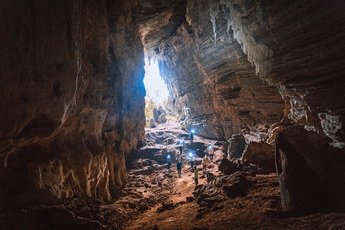 Group of people walking in large cave with sunlight from behind