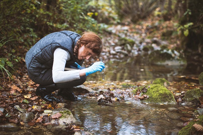 Woman Biological Researcher Taking a Water Sample from a stream.