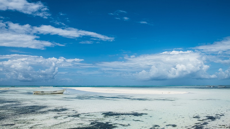 Lone boat in clear ocean water under a blue sky with clouds