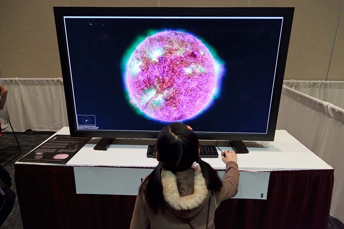 Young girl looking at space graphic on monitor and interacting with computer 