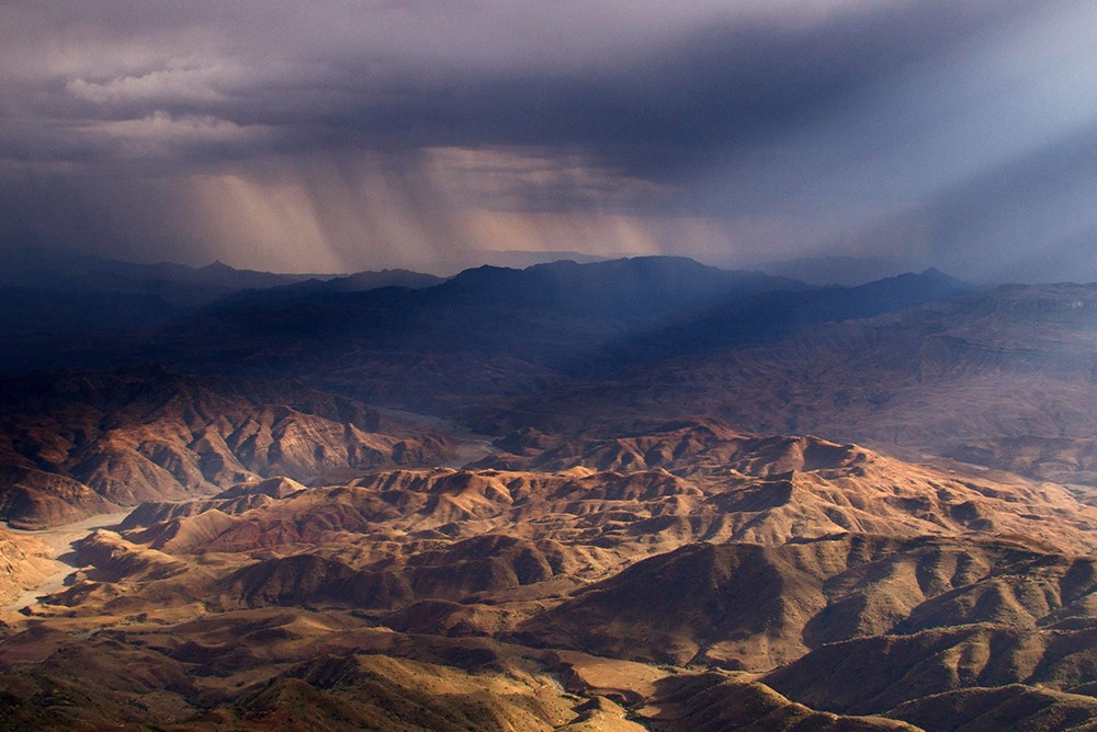 Hills with sunbeam and dark storm clouds in distance