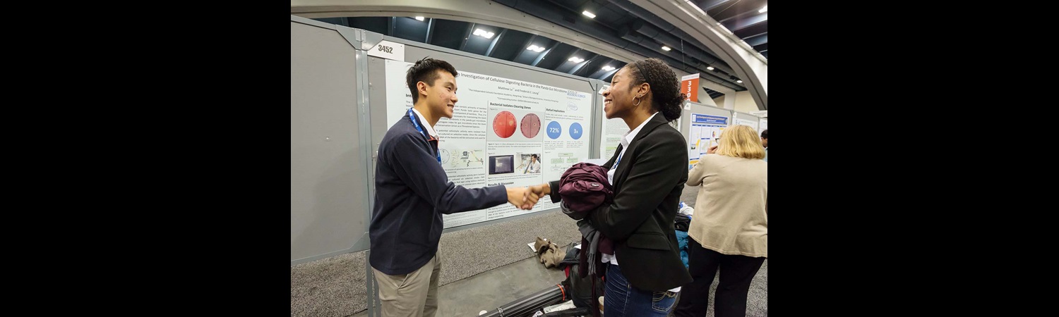 Two students shaking hands in poster hall Two students shaking hands in poster hall