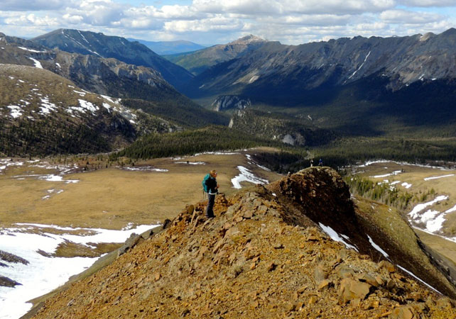 Woman standing on rocky hill with mountains and melting snow in the background
