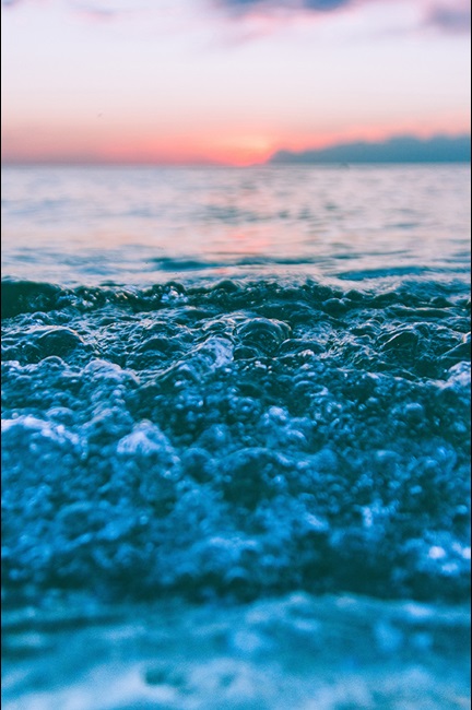 Ocean waves with foam and sunset background