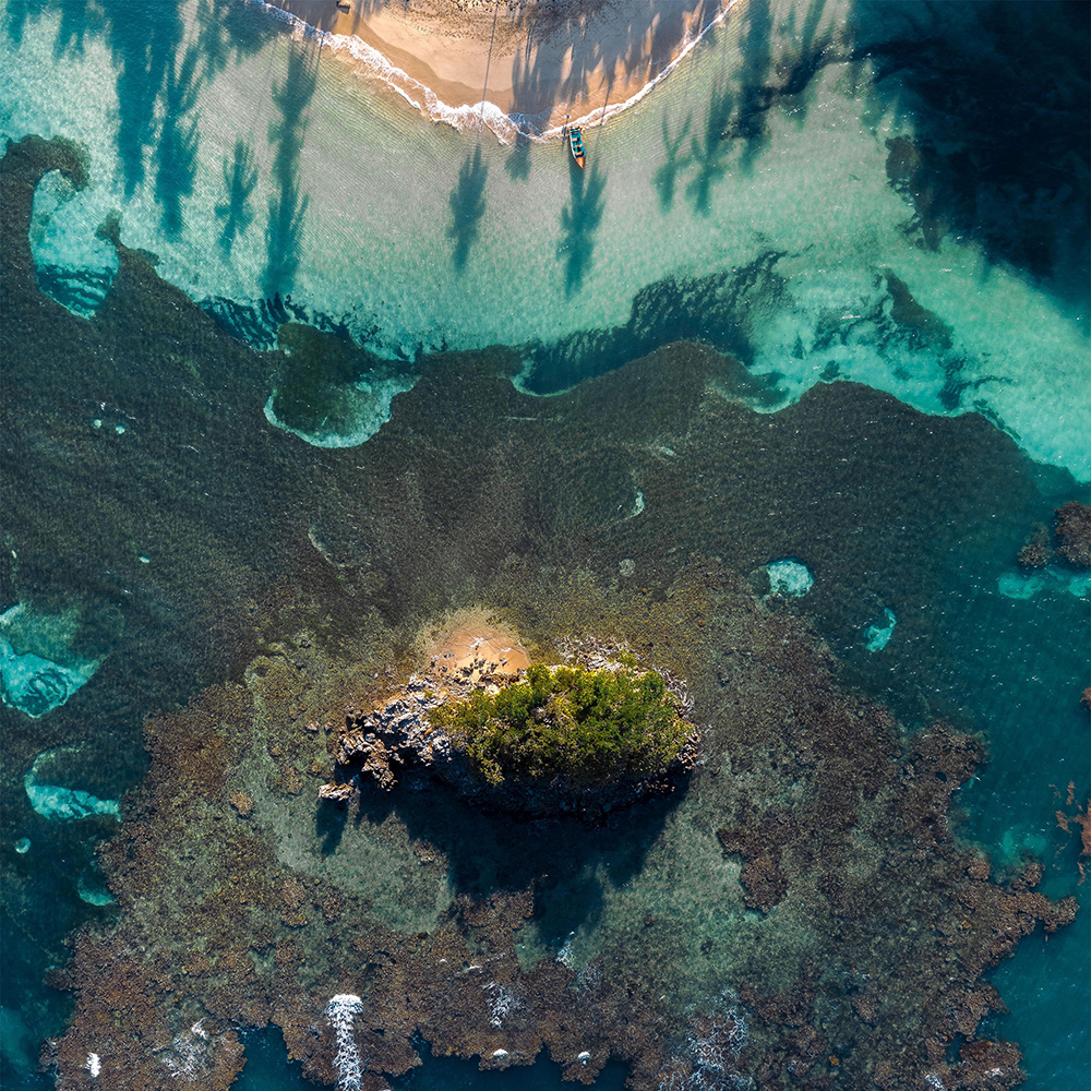 Aerial view of a tropical beach with coral and a boat at the waters edge. 
