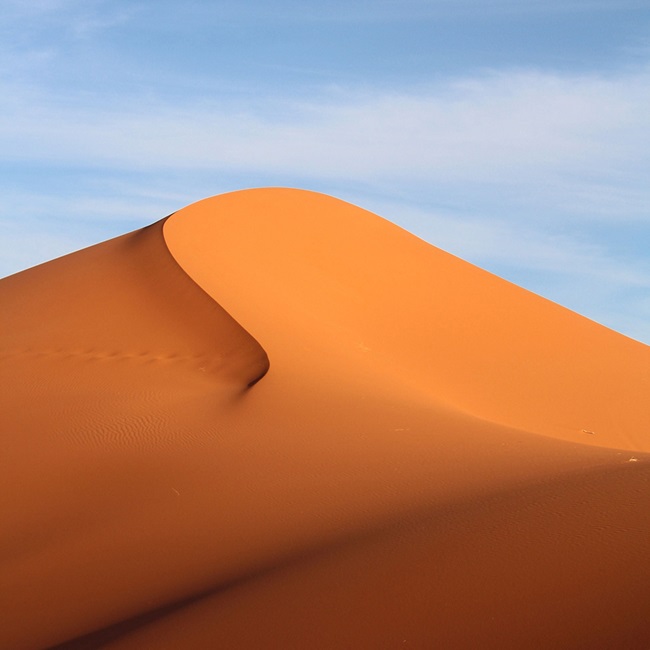 a large dramatic sandy dune with blue sky behind it