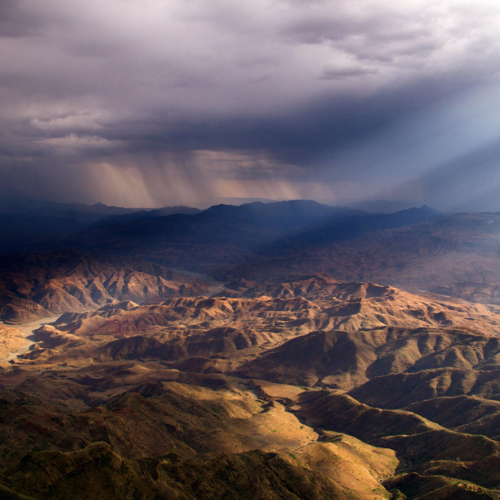Hills with sunbeam and dark storm clouds in distance