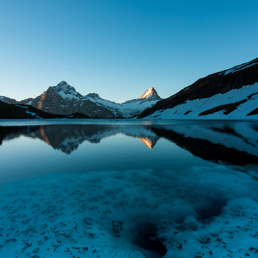 looking across a cold alpine lake at snow capped mountains