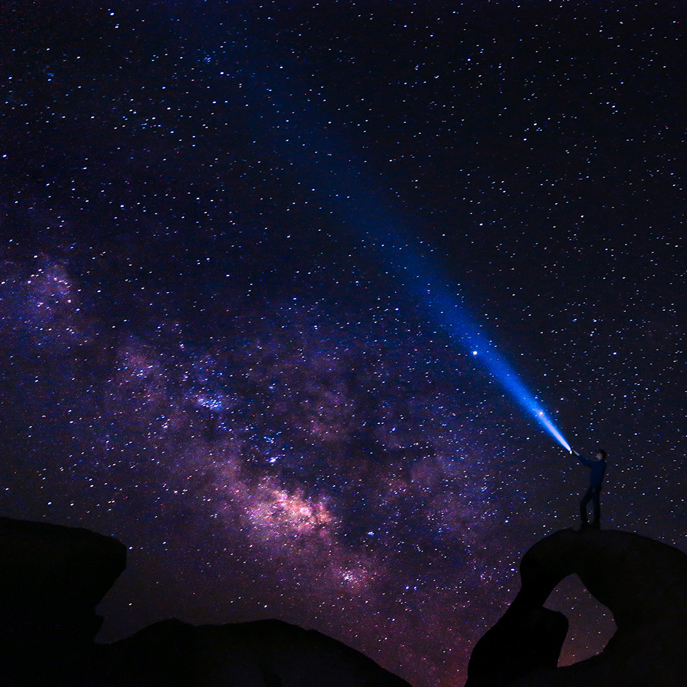 Person shining flashlight on the stars in the sky