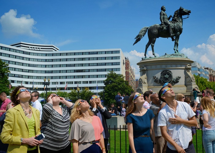 People looking up at the sky, wearing solar eclipse glasses.