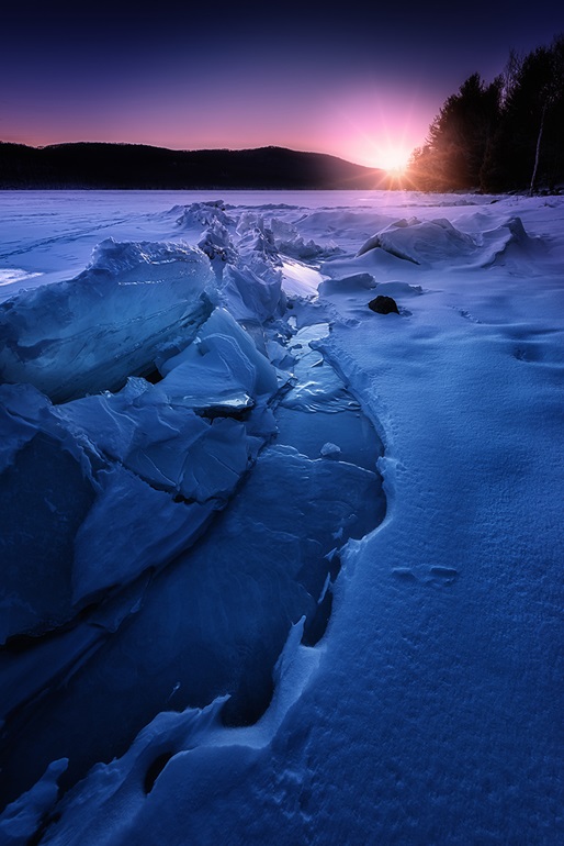 Sun rising over ice and snow covered stream
