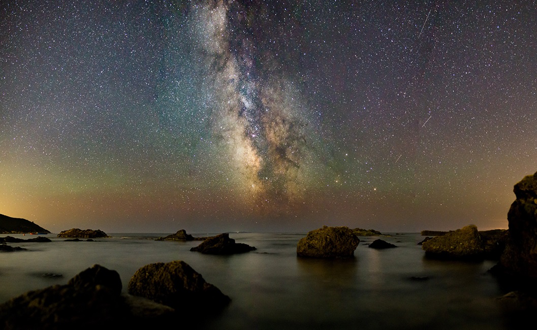 Rocks in water at night with galaxy sky