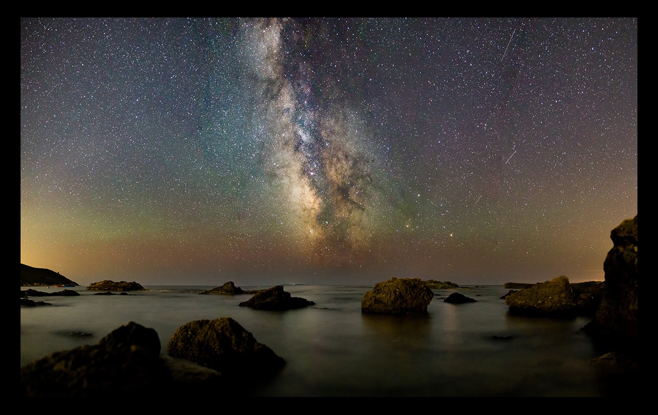 Rocks in water at night with galaxy sky