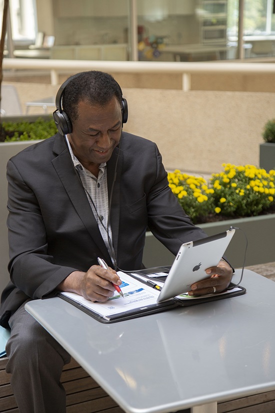 Man with headphones, holding ipad, and writing on worksheet woman smiling
