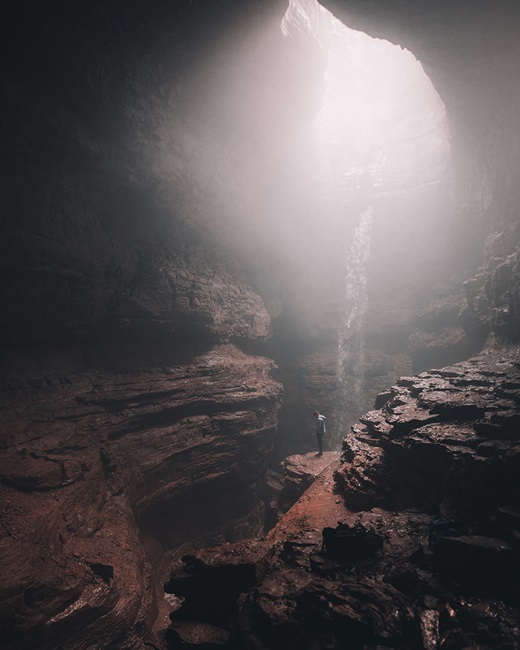 Person standing in deep cave with sunlight from above