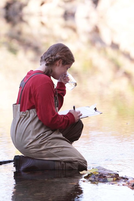 Young woman recording data from water sample in creek