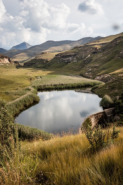 Green mountains and grassland surrounding a small pond